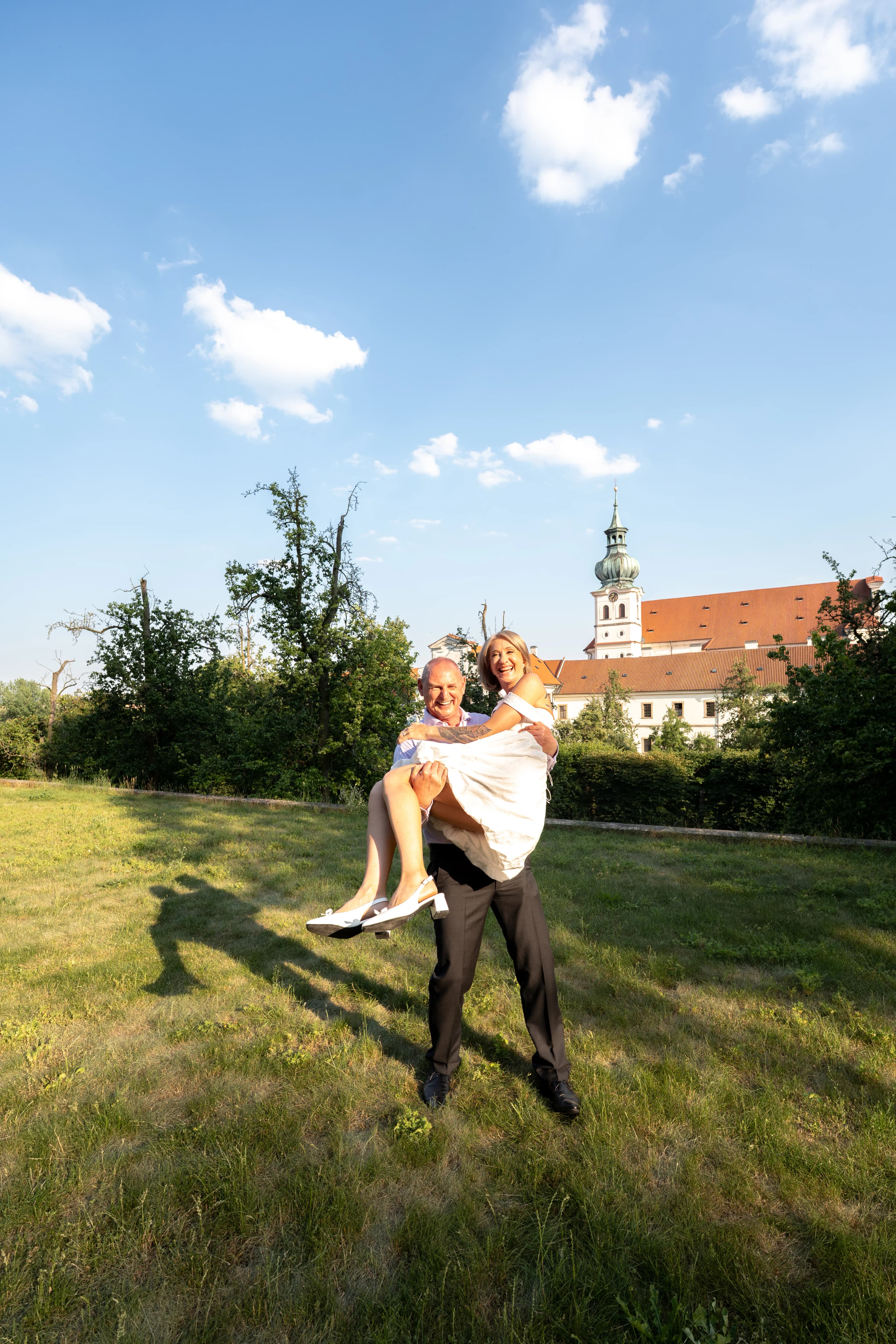 Couple de mariés joyeux devant le monastère de Prague sous un ciel bleu, photographe de mariage Prague Clément Bayard